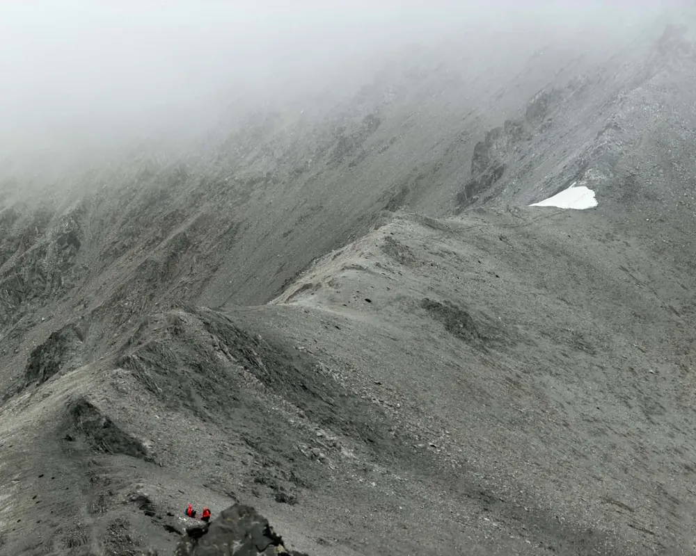 Two hikers in red jackets crossing a steep rocky scree slope in mist